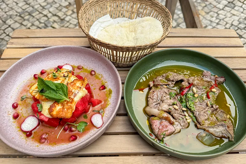 Numa mesa da esplanada, halloumi com melancia e romã, fatias de carne em molho com pinhões e malagueta, e um cesto de pão